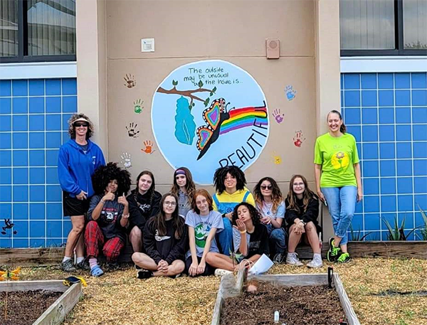 Former students led a community service project to paint a mural on the wall of the Dunedin Elementary school garden.